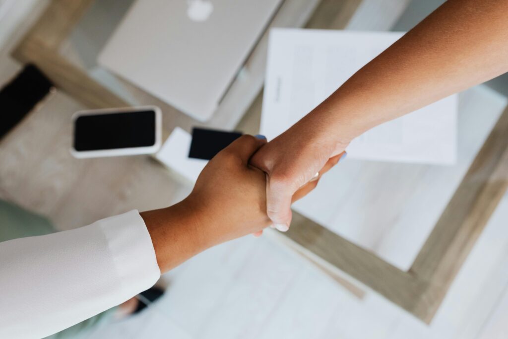 Two people shaking hands over a desk with modern tech, symbolizing a successful business agreement.